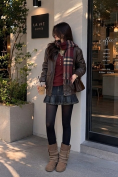 Woman in a brown leather jacket and plaid scarf outside a coffee shop