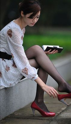 Woman in a polka dot dress and black pantyhose adjusting her red heels outdoors