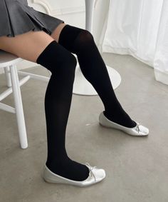Person wearing a pleated skirt, thigh-high socks, and silver flats while sitting
