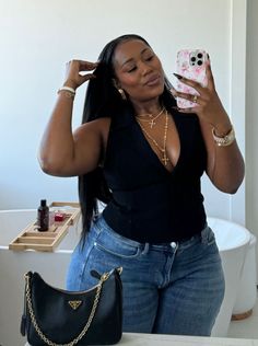 Woman in a black top and blue jeans taking a mirror selfie in a bathroom
