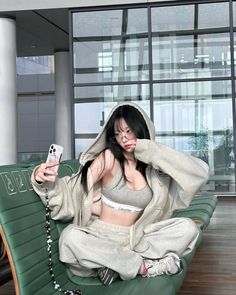 Woman in a grey hoodie and sports bra sitting indoors with a phone