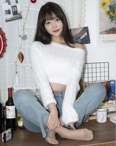 Woman with long hair wearing a white off-shoulder sweater and jeans, sitting indoors