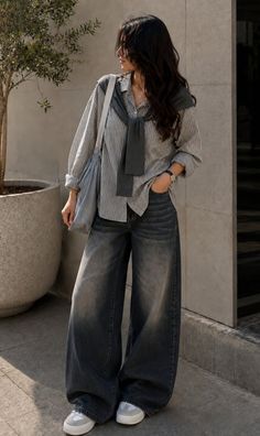 Woman in a striped shirt and wide leg jeans with a sweater over her shoulders
