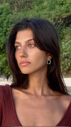 Woman with long dark hair and green eyes wearing a red top outdoors
