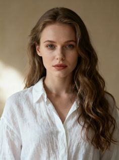 Woman with long wavy hair wearing a white shirt, looking directly at the camera