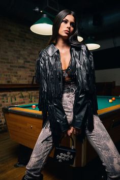 Woman in a fringe jacket and snakeskin pants posing by a billiards table