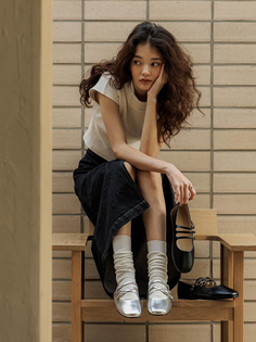 Woman with long wavy hair sitting outdoors, holding a black shoe