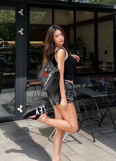 Woman in a black tank top and denim shorts posing outdoors