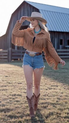 Woman in a cowboy hat, fringe jacket, and denim shorts outdoors at golden hour