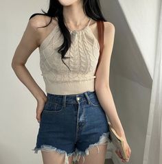 Person in a knitted halter top and denim shorts holding a book