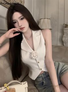 Woman with long dark hair wearing a white vest and denim shorts indoors