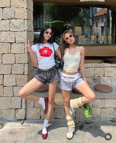Two young women posing in front of a stone wall and shop window