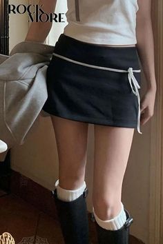 Person in a black mini skirt, white crop top, and long boots indoors