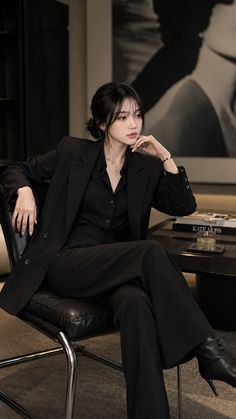 Woman in a black suit sitting indoors with a thoughtful expression