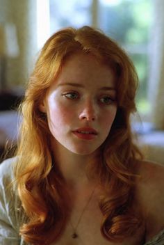 Woman with long red hair and exposed shoulders wearing a necklace indoors