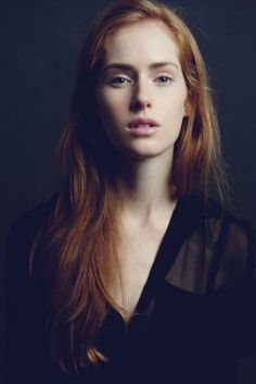 Woman with long red hair wearing a sheer black top, upper body portrait