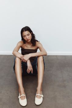 Woman with dark hair wearing a strapless top and denim skirt, sitting on the floor