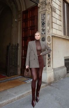 Woman in a plaid blazer, mini skirt, and brown tights on a city street