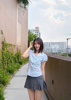 Woman in a light blue shirt and pleated skirt outdoors with a cityscape background