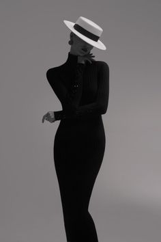 Woman in a black ribbed dress and white hat posing in a studio