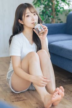 Woman with long hair sitting on a wooden floor, drinking from a bottle