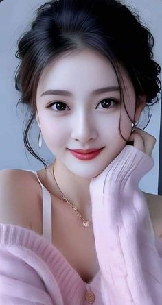 Woman with black hair in an updo wearing a pink sweater and gold necklace