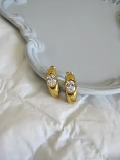 Pair of gold hoop earrings with oval gemstones on white fabric and a light blue tray