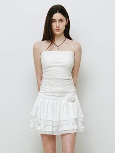 Woman with long dark hair wearing a white dress with spaghetti straps and a ruffled skirt