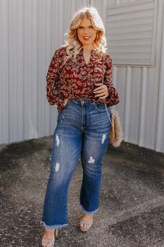 Woman with blonde hair wearing a floral blouse and distressed jeans outdoors
