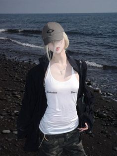 Person with blonde hair and a baseball cap on a dark pebble beach