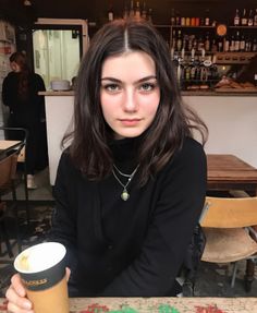Woman with long dark hair in a black top holding a coffee cup in a cafe