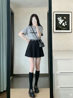 Woman in a gray t-shirt and black pleated skirt taking a mirror selfie