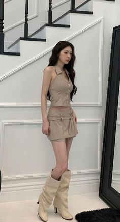 Woman in a beige crop top and mini skirt with tall boots indoors