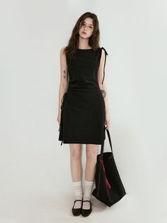 Woman in a black dress and glasses holding a tote bag against a white background