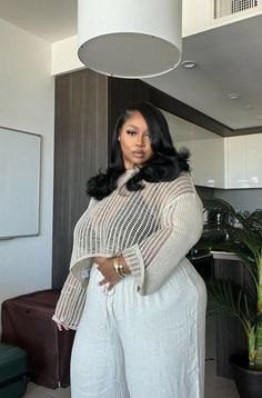 Woman with long dark hair wearing a crochet top and wide leg pants indoors