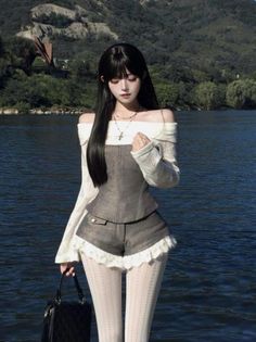 Woman with long black hair wearing an off-shoulder top and shorts by a lake