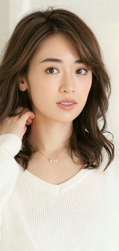 Woman with brown wavy hair wearing a white sweater and necklace