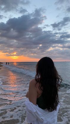 Woman with long dark hair looking at the sunset over the ocean