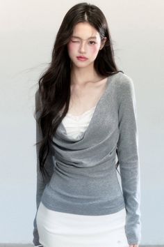 Woman with long dark hair winking in a grey top and white skirt
