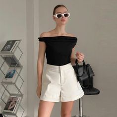 Woman in an off-shoulder top and white shorts holding a black handbag