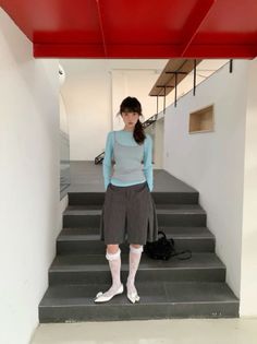 Woman in a blue top and culottes standing on stairs in a minimalist indoor setting