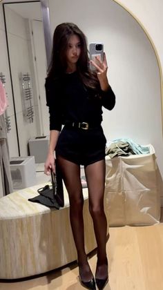 Woman in a black top and shorts with tights taking a mirror selfie