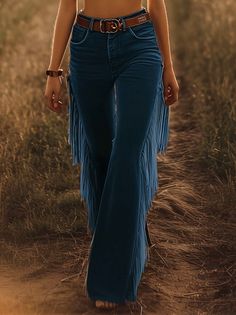 Person in denim jeans with fringe and a brown belt walking on a path