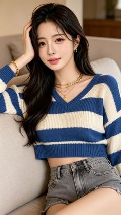 Woman with long dark hair wearing a striped sweater and denim shorts indoors