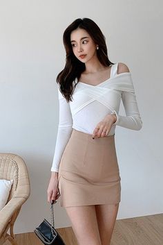 Woman with long dark hair wearing a white top and a beige mini skirt indoors
