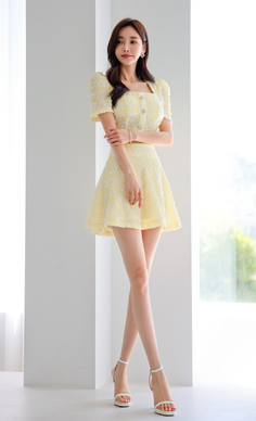 Woman in a yellow dress and white heels posing indoors