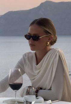 Woman in sunglasses and a white top dining outdoors with a mountain view