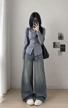 Person with long black hair in a striped shirt and wide leg jeans taking a mirror selfie