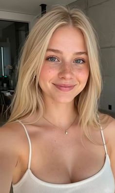 Blonde woman with blue eyes and freckles wearing a white top and necklace
