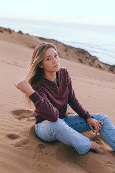 Woman with blonde hair sitting on sand dunes with the ocean in the background